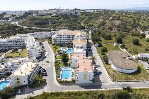 Vista aérea do hotel RB Algarve em Albufeira com piscina, edifícios brancos, paisagem verde e áreas de estacionamento