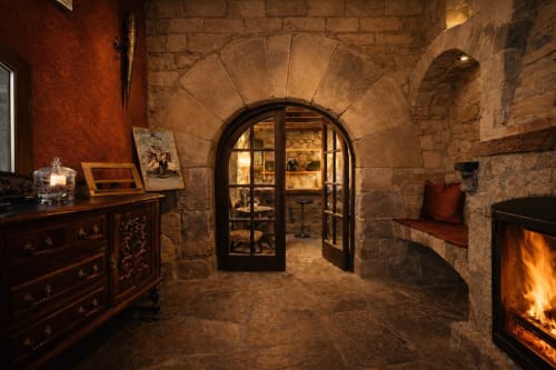Sala de piedra con chimenea y puerta arqueada de madera junto a mobiliario clásico.