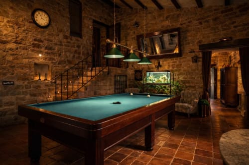 Sala de piedra con mesa de billar, escalera metálica y vigas de madera.