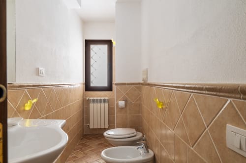 Bagno moderno con piastrelle a rombi beige, lavabo bianco, bidet e wc all'hotel Youinsardinia a Bari Sardo, Italia