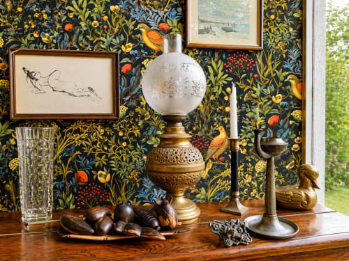 Ornate desk display at La Villa Malzy featuring decorative wallpaper, framed artwork, brass lamp, and collected objects in