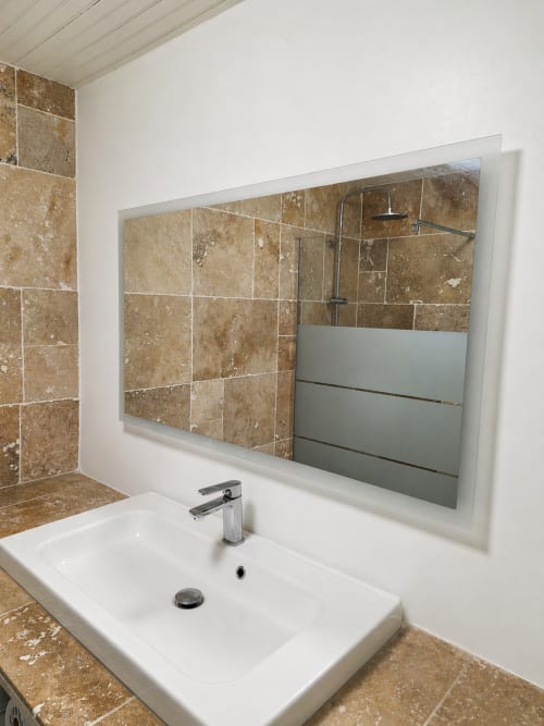 Modern bathroom at La Villa Malzy with travertine tile, white sink, and framed mirror
