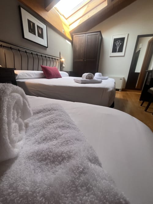 Dreibettzimmer im CasaAzcona mit zwei Betten, weißer Bettwäsche, burgunderrotem Kissen und Dachfenstern im Dachgeschoss
