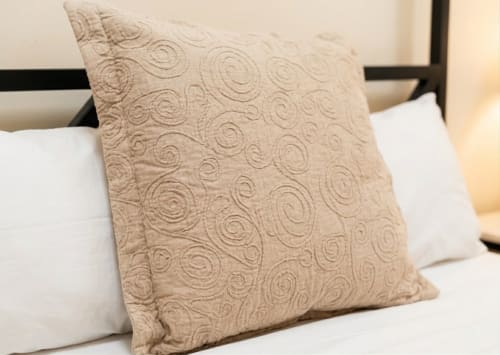 Un cojín decorativo acolchado beige con patrón de espiral en la cama de Villa M