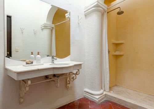 El baño de una villa con lavabo blanco, columna decorativa, área de ducha amarilla y piso de terracota en Villa Hotel en México