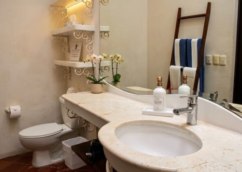 Un baño moderno en Villa Merit de un hotel boutique en México con lavamanos de mármol, espejo iluminado y toallas decorativas