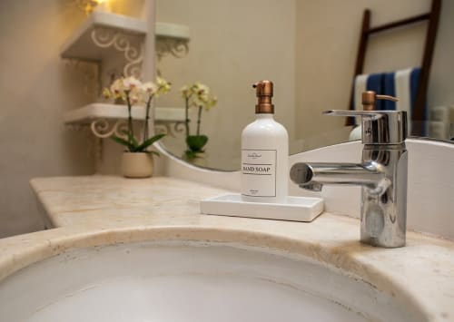 El lavamanos del baño de la villa con jabón de manos, grifo y flores decorativas sobre una encimera de mármol