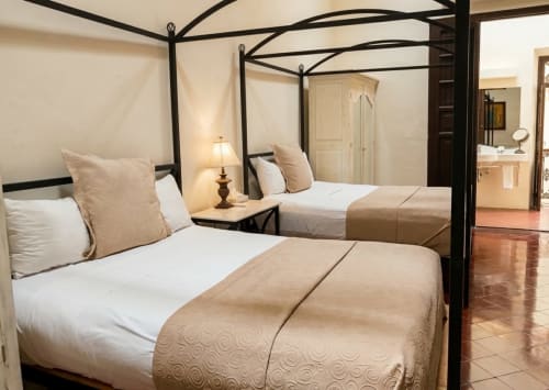 Los dos camas dobles con dosel, sábanas blancas y mantas color beige en el hotel boutique Villa merida de mérida