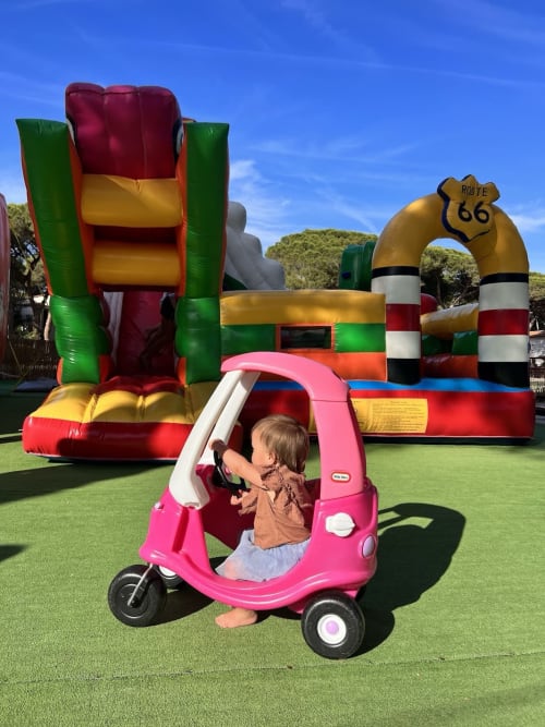 Child in pink toy car at Casa P ineta play area, Marina di Campo, with colorful inflatables and Route 66 obstacle course