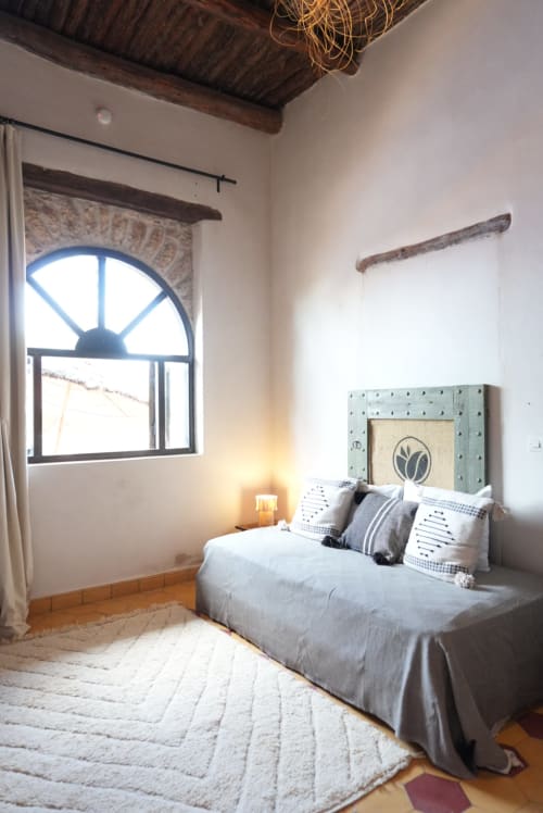 Vue de la chambre moderne d'une maison d'hôtes avec fenêtre cintrée, vue sur la piscine, literie grise et poutres en bois rustique