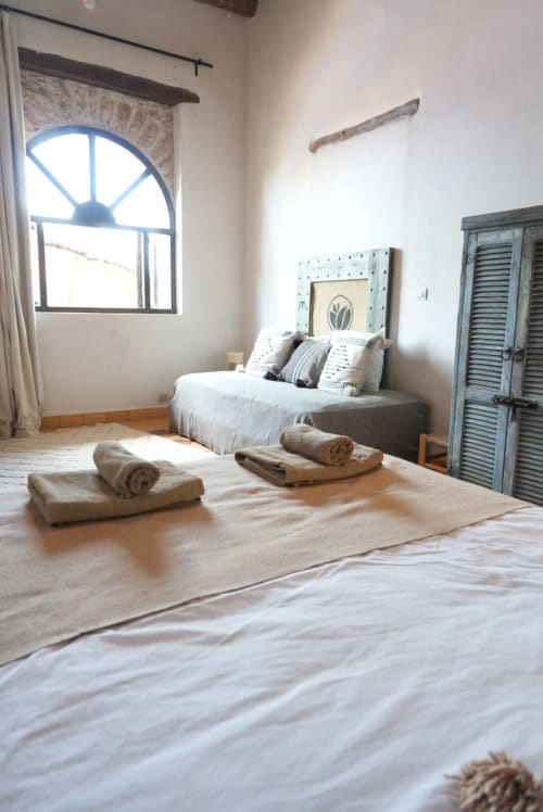 De la clarté dans une chambre de gîte avec deux lits, serviettes roulées, fenêtre cintrée, décor rustique et armoire à volets verts