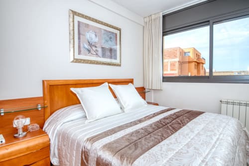 Modern bedroom at Hotel with wood bed, white pillows, brown bedding, and city view window in Es