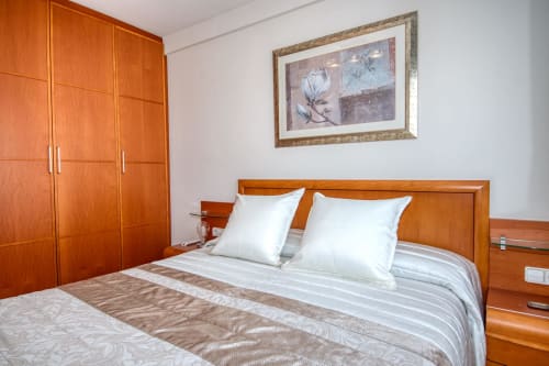 Modern bedroom at Hotel with wooden furnishings, white pillows, striped bedding, wardrobe, and framed floral artwork
