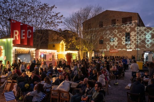 La multitud vespertina a l'espai d'events a l'aire lliure de l'Hotel Can Carol a Barcelona, amb un ambient de mercat animat i taules per menjar