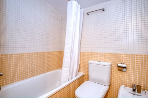 Modern bathroom at Hotel with white and orange tile walls, bathtub with shower curtain, toilet and sink fixtures