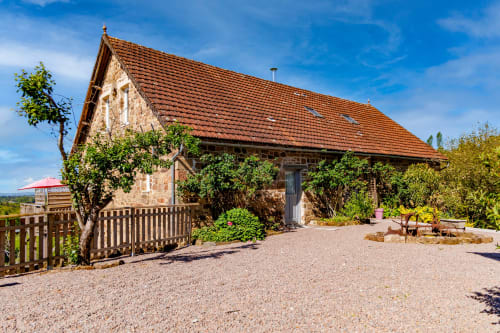La maison d'hôtes Les instants volés à tudeils : façade en pierre, toit en tuiles, lierre, clôture en bois et cour en gravier