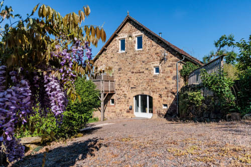 Le gîte en pierre avec glycine violette aux Les-InstantsVolés B&B dans un village français rural, ciel bleu dégagé