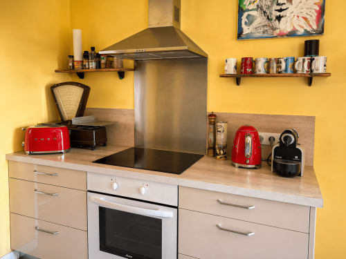 Modern kitchen at La Villa hospitality with yellow walls, stainless steel range hood, red appliances, and wooden cabinetry