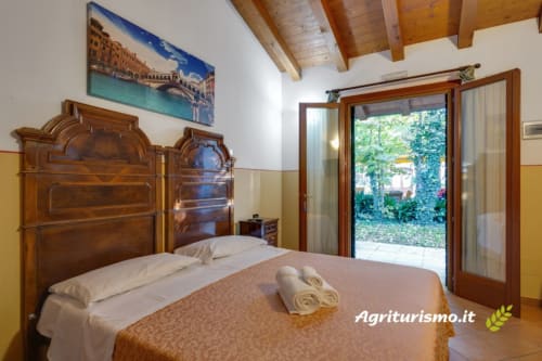 Camera matrimoniale con letto in legno, vista giardino e travi a vista in Villa in campagna toscana