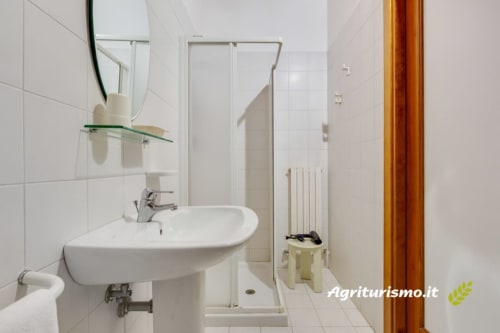 Il bagno moderno con piastrelle bianche, lavabo curvo, specchio e box doccia di questo agriturismo italiano