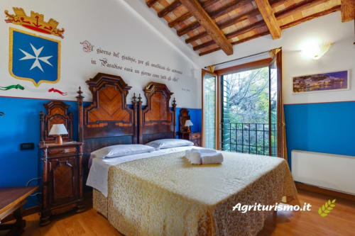 Camera tripla in agriturismo con arredi in legno, pareti blu, travi in cotto e vista sul giardino in Italia
