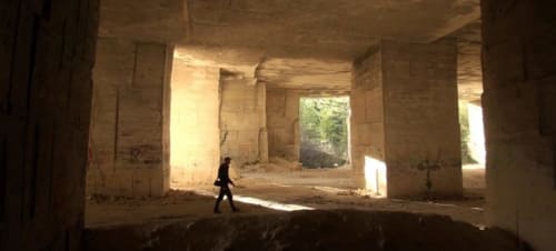 Person exploring abandoned interior space at rural French property with stone columns and natural light