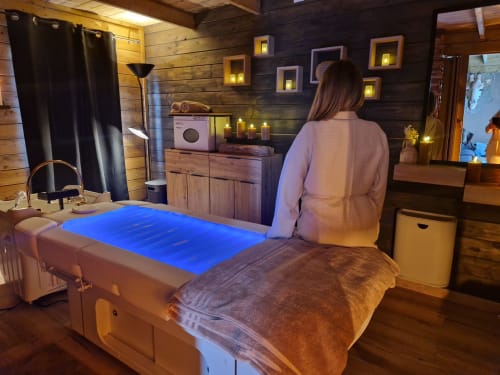 Client relaxant dans la chambre spa zen du gîte À L'offre zen avec lit de massage illuminé en bleu et éclairage ambiant, intérieur boisé, France