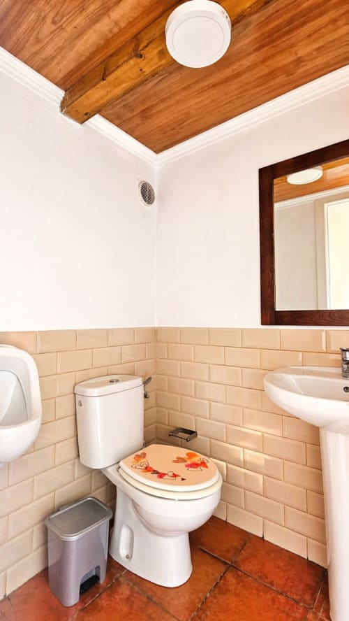 Casa de villa La aldea: baño moderno con azulejos tipo metro beige, vigas de madera en techo, lavabo pedestal y asiento de inodoro decorativo
