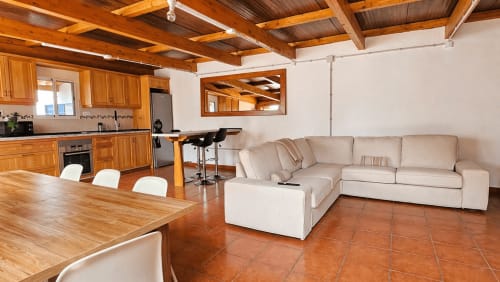 Villa de concepto abierto con vigas de madera, sofá beige, comedor y cocina moderna en La aldea