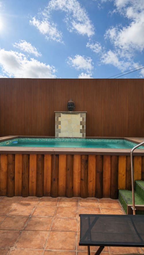 Una moderna piscina climatizada con agua turquesa, terraza de madera, pared de metal ondulado y estatua de buda en Villa DR de La AldeaHotel
