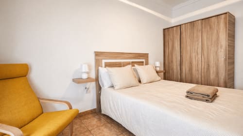 El moderno dormitorio de Villa DR en La aldea, con cama de madera, cómodo sillón amarillo y muebles de madera con vistas a la montaña