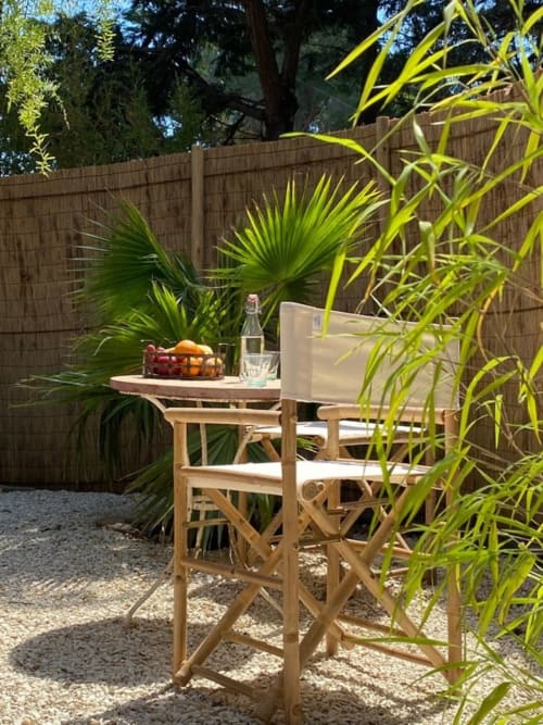 Sunny outdoor dining area at Le Patio aux Oiseaux B&B in La Ciotat with wooden table, tropical plants, and wine bottle