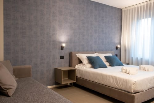 Camera da letto moderna presso SMalL Guesthouse a Bussolengo con cuscini blu, biancheria neutra e pareti grigie texture