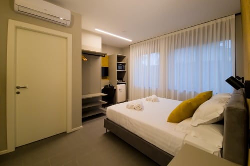 Camera da letto moderna presso SMalL Guesthouse a Bussolengo con letto bianco, cuscino giallo e tende da pavimento a soffitto