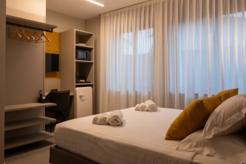 Camera Ambra presso SMalL Guesthouse a Bussolengo, Italia con letto matrimoniale, cuscini dorati, scrivania, mensole e tende trasparenti