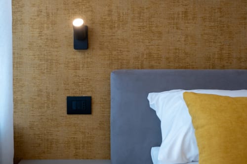 Camera da letto moderna in SMalL Guesthouse, Bussolengo con letto grigio, cuscini gialli, parete texture e illuminazione contemporanea