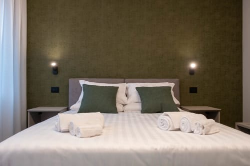 Camera Malachite presso SMalL Guesthouse Bussolengo con letto queen, cuscini verdi, asciugamani arrotolati e illuminazione ambientale a parete