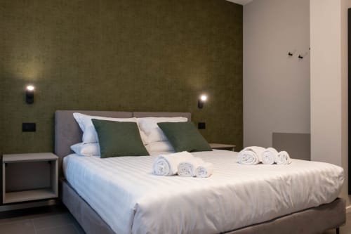 Camera moderna presso SMalL Guesthouse a Bussolengo con pareti color oliva, letto con cuscini verdi, asciugamani arrotolati e atmosfera accogliente