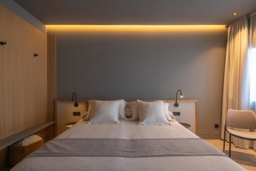 Camera moderna dell'hotel The Alma Suite in Spagna con letto queen, illuminazione ambientale e tende con vista giardino