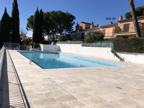 Resort swimming pool at Capleouna, Cap d'Antibes, with Mediterranean villas and cypress trees under clear blue sky