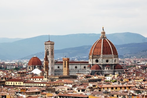 Cattedrale di Firenze con cupola rossa e campanile che si ergono sopra i tetti in terracotta, le montagne toscane sullo sfondo