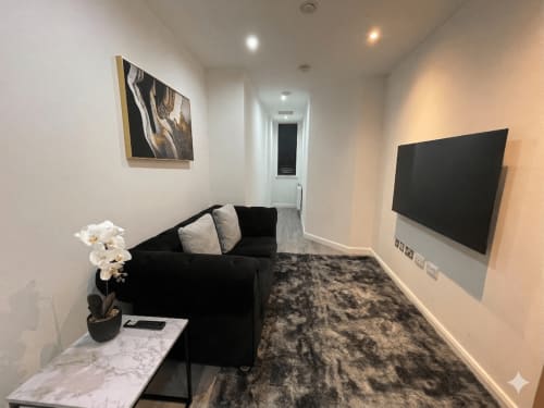 Modern apartment lounge with black sofa, wall-mounted TV, marble table and orchid plant at Empire Serviced Apartments