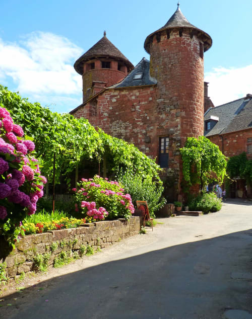 Château en pierre rouge avec tours entouré de fleurs roses en fleur aux Instants Volés à Tudeils, France