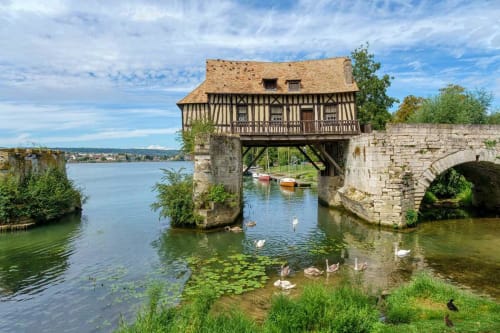 Historic watermill at La Villa Malzy in Vétheuil with stone bridge, timber-framed building and swans in river