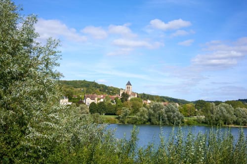 Vétheuil village with church overlooking the Seine river, surrounded by lush greenery and trees