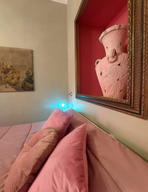 Literie rose dans la Suite du Palazzo Losio avec lampe bleue et sculpture en relief encadrée sur mur rouge