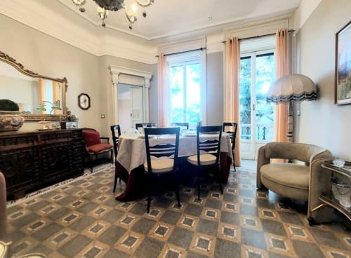 Élégante salle à manger de la suite Palazzo Losio avec table ronde, chaises noires, cheminée et vue sur le jardin par grandes fenêtres