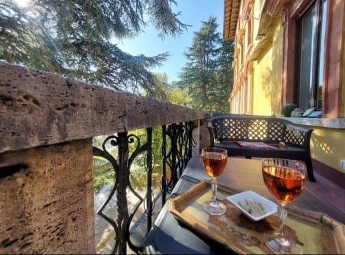 Terrasse élégante du Palazzo Losio avec balustrade en fer forgé, verres à vin, vue sur collines boisées et bâtiment historique en pierre