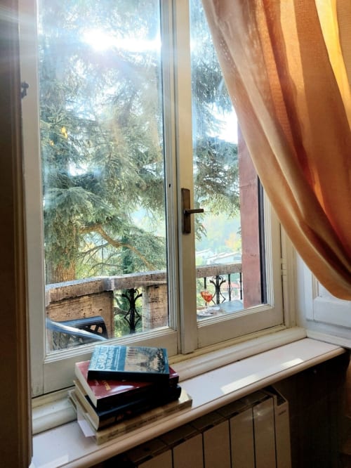 Fenêtre ensoleillée avec livres sur le rebord, vue sur le jardin, rideaux orange dans la suite Palazzo Losio, Ponzone Italie