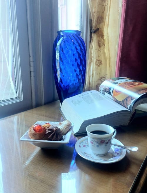 Coin de lecture douillet au Palazzo Losio avec vase bleu, café, pâtisseries et livres surplombant le Piémont